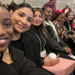 A joyful group photo shows two women sitting, one in a floral top, the other in a wheelchair with a beige shirt, and a smiling man standing behind them in a room. Description:  TEDx Largo rehearsal event at Creative Suitland.