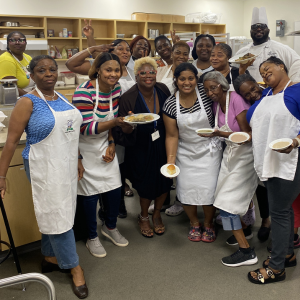 A group of seven men posing together in the Washington Commanders parking lot on a sunny day. Some are wearing sports jerseys, and one is in a wheelchair, smiling contently.  Description: Pre season fun at a Washington Commanders game.