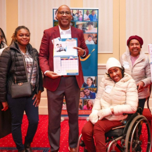 A group of seven people smiling inside the Maryland General Assembly. Two individuals hold calendars. One person is in a wheelchair. 