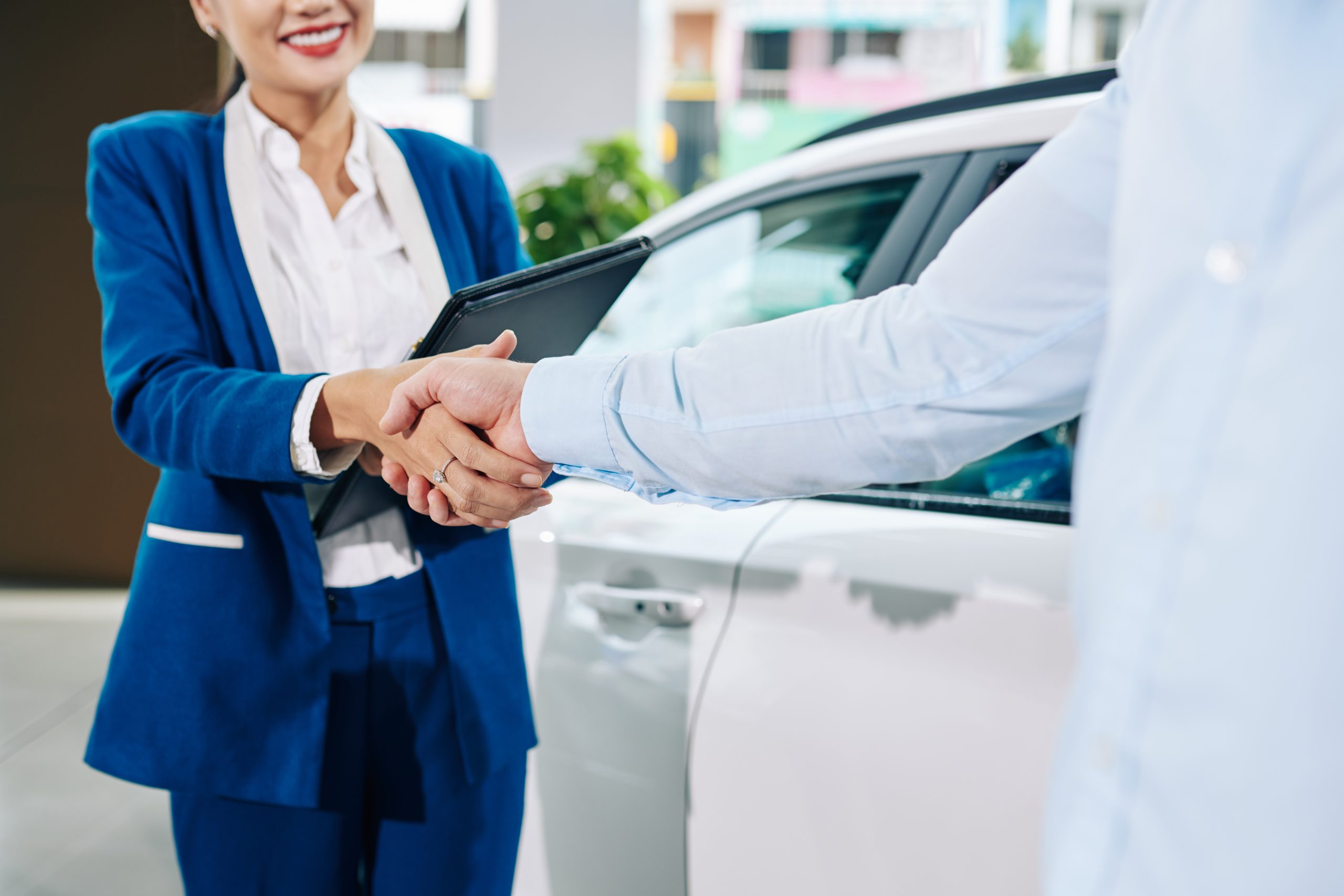 Two people shake hands beside a vehicle, representing a completed vehicle donation or charitable contribution.